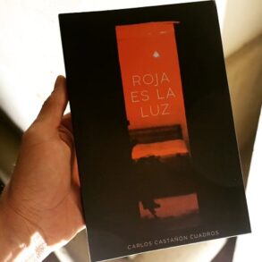 UNA MANO SOSTIENE EL LIBRO 'ROJA ES LA LUZ' DE CARLOS CASTAÑÓN